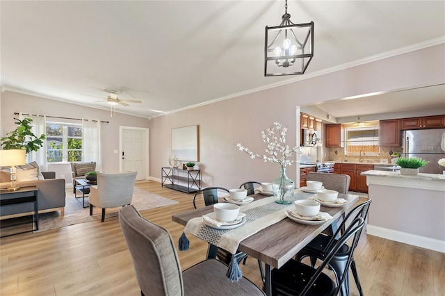 dining area with light wood-type flooring, baseboards, crown molding, and ceiling fan with notable chandelier