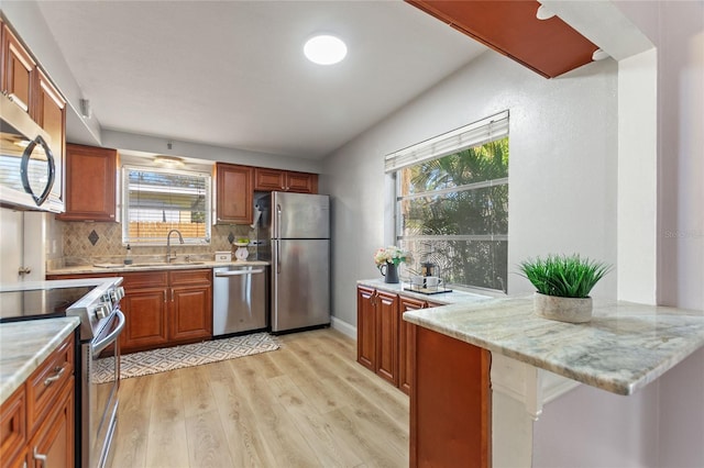 kitchen featuring light wood finished floors, decorative backsplash, brown cabinetry, a peninsula, and stainless steel appliances