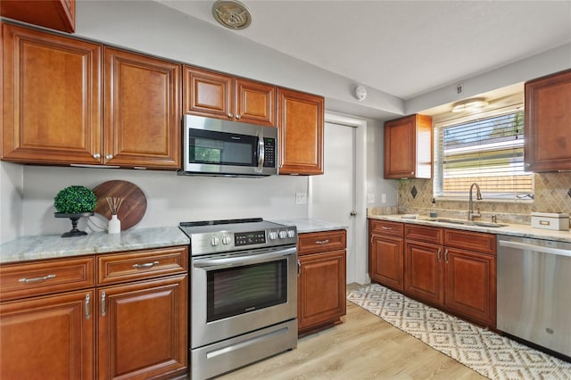 kitchen featuring a sink, light wood-style floors, appliances with stainless steel finishes, decorative backsplash, and brown cabinets