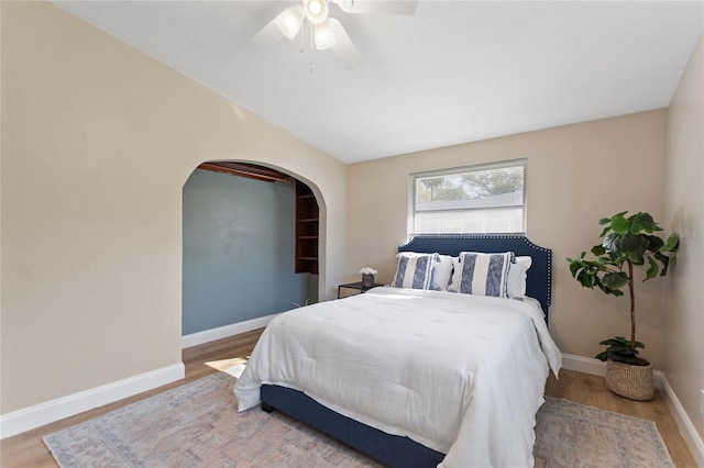 bedroom with baseboards, arched walkways, ceiling fan, and wood finished floors