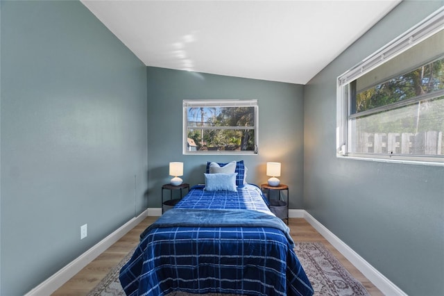 bedroom with baseboards, vaulted ceiling, and wood finished floors