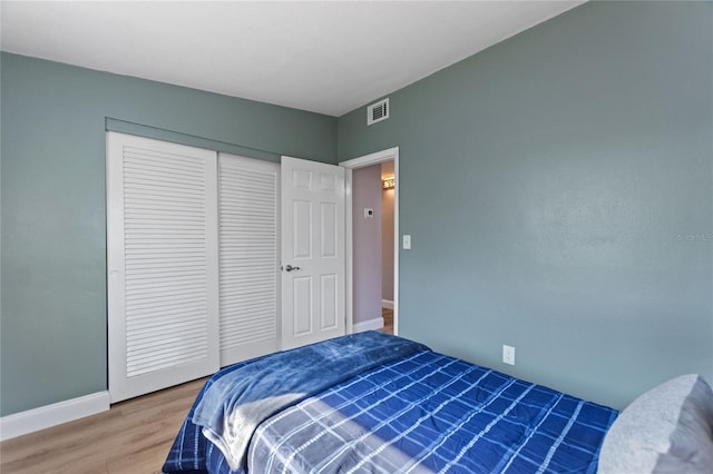 bedroom with baseboards, a closet, visible vents, and wood finished floors