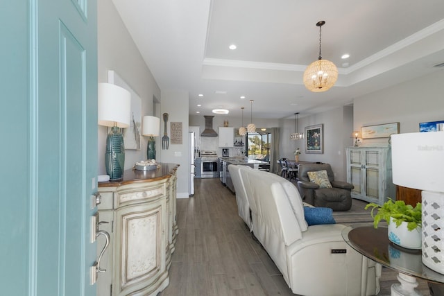 living room featuring crown molding, recessed lighting, a raised ceiling, an inviting chandelier, and wood finished floors