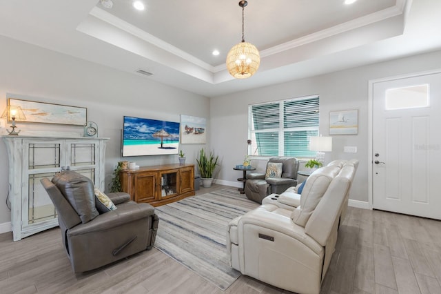 living room featuring light wood-style flooring, visible vents, baseboards, ornamental molding, and a tray ceiling