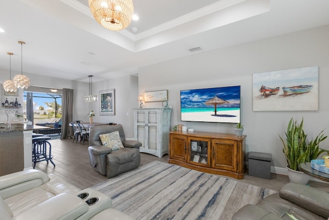 living room featuring a chandelier, a raised ceiling, visible vents, and wood finished floors