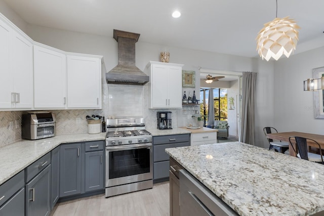 kitchen featuring stainless steel gas range oven, light stone countertops, premium range hood, white cabinetry, and backsplash