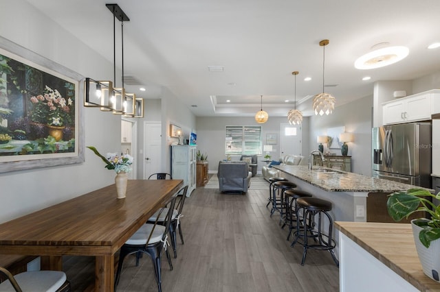 dining space featuring baseboards, a raised ceiling, light wood-style flooring, and recessed lighting