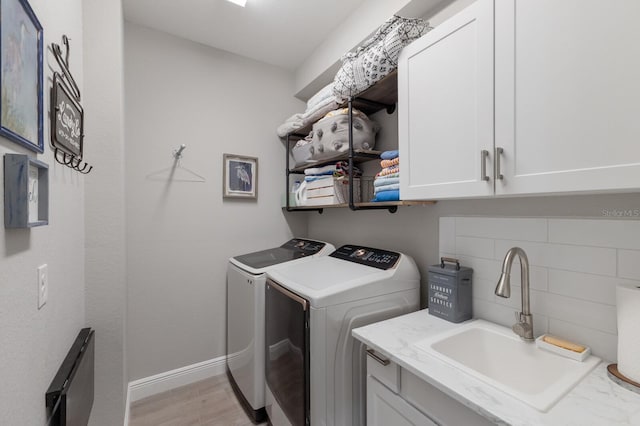 washroom featuring cabinet space, light wood finished floors, baseboards, washer and clothes dryer, and a sink