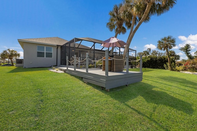 rear view of property featuring glass enclosure, a lawn, a wooden deck, and stucco siding