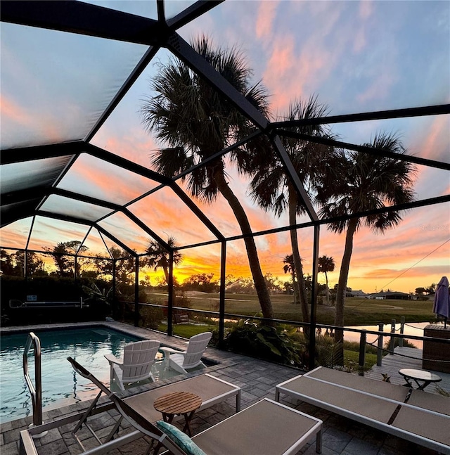 pool at dusk with glass enclosure, a patio area, and an outdoor pool