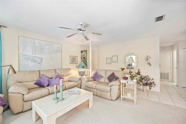 living area featuring light tile patterned floors, visible vents, a textured ceiling, and a ceiling fan