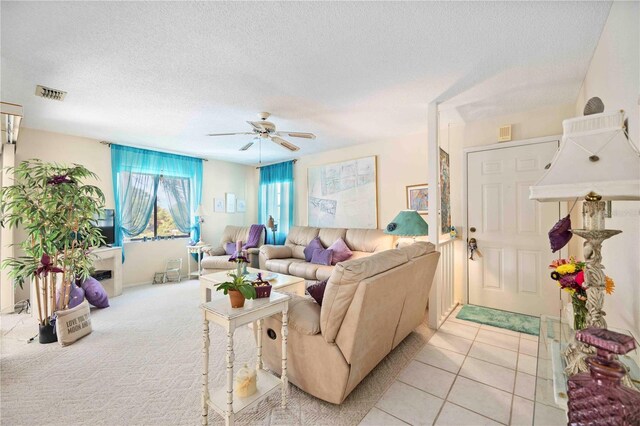 living room with visible vents, a ceiling fan, a textured ceiling, light tile patterned flooring, and light colored carpet