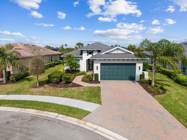 view of front of home featuring a tile roof, an attached garage, decorative driveway, a front yard, and stucco siding