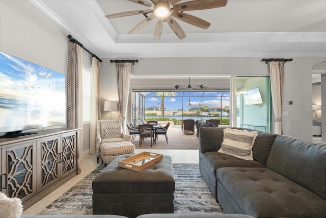 living area with ornamental molding, arched walkways, a raised ceiling, and a ceiling fan