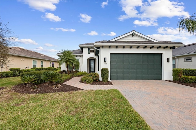 view of front facade with an attached garage, a tiled roof, decorative driveway, stucco siding, and a front yard