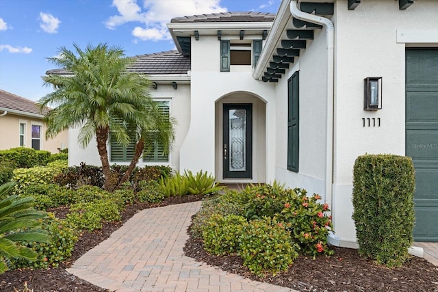 entrance to property with a garage, a tile roof, and stucco siding