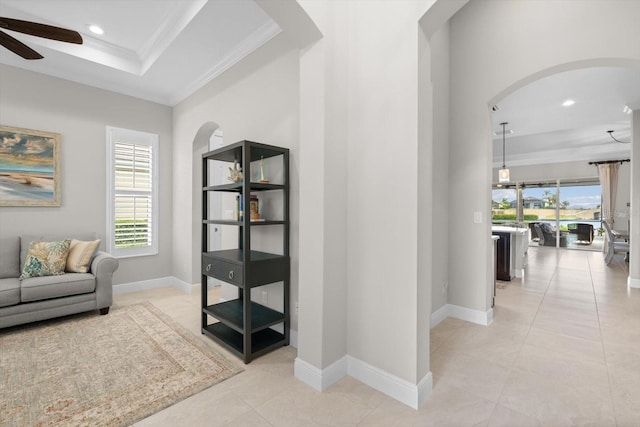 hall featuring light tile patterned floors, baseboards, arched walkways, a tray ceiling, and crown molding