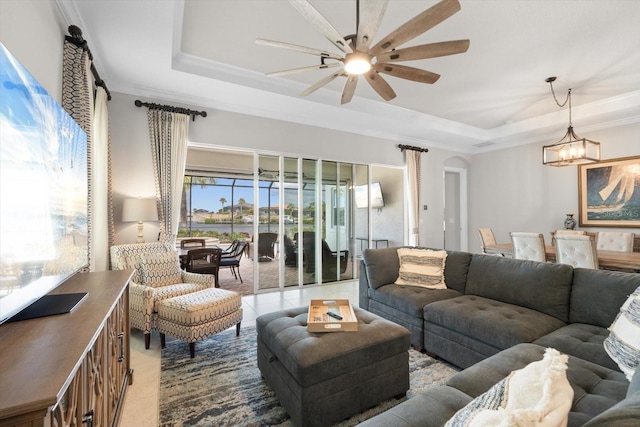 living room featuring a tray ceiling, arched walkways, crown molding, and ceiling fan with notable chandelier