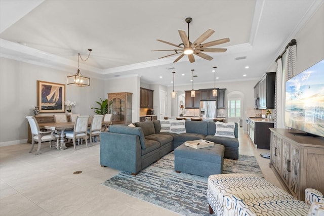 living room featuring light tile patterned flooring, ornamental molding, a raised ceiling, and ceiling fan with notable chandelier