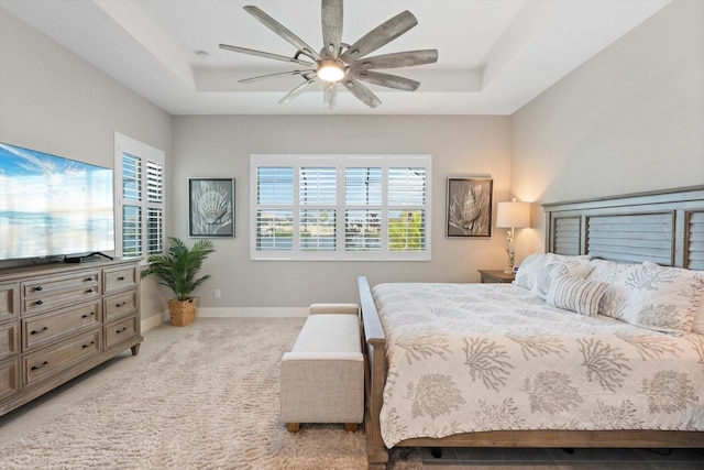 bedroom featuring baseboards, a tray ceiling, a ceiling fan, and light colored carpet