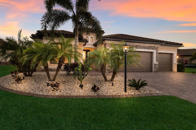 view of front of property with decorative driveway, stucco siding, a front yard, a garage, and stone siding