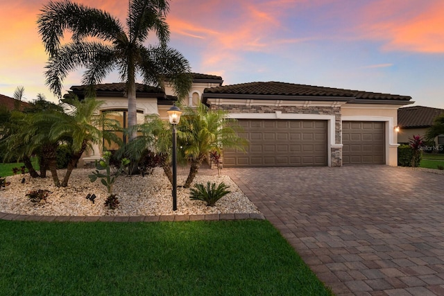 mediterranean / spanish-style home featuring a garage, decorative driveway, stone siding, and stucco siding