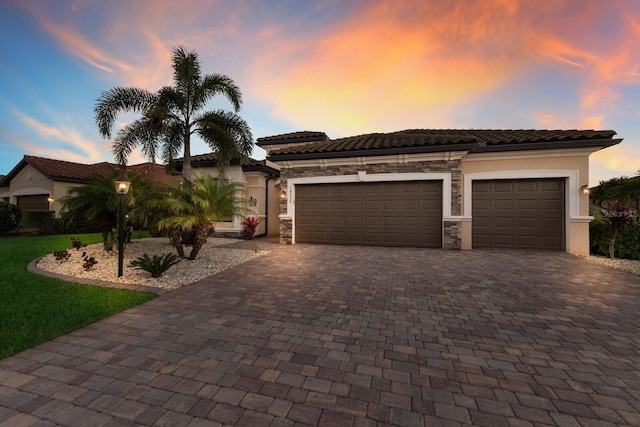 view of front facade with a garage, stone siding, a tiled roof, decorative driveway, and stucco siding