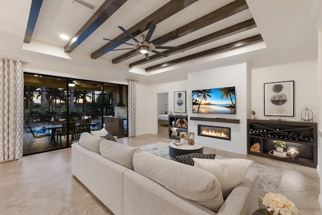 living area with beamed ceiling, a glass covered fireplace, visible vents, and a ceiling fan