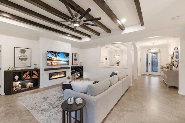 living room with arched walkways, beamed ceiling, and a glass covered fireplace