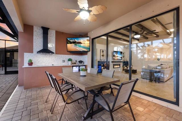 dining room with brick floor, a warm lit fireplace, ceiling fan, and a wood stove