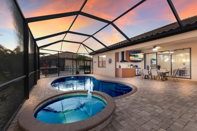 pool at dusk with glass enclosure, a patio area, and a pool with connected hot tub