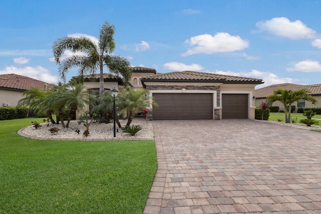 mediterranean / spanish-style home featuring decorative driveway, stucco siding, an attached garage, a front yard, and stone siding