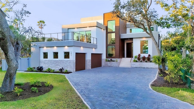 modern home featuring decorative driveway, stucco siding, a front yard, a balcony, and a garage