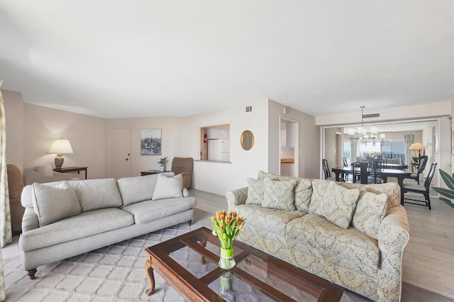 living area featuring visible vents, light wood-style floors, and an inviting chandelier