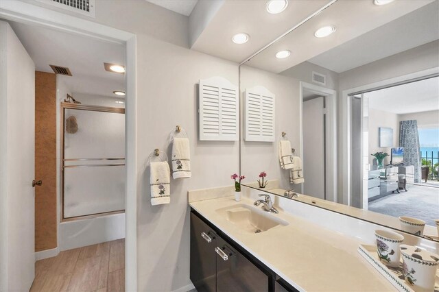 full bath with visible vents, combined bath / shower with glass door, vanity, and wood finished floors
