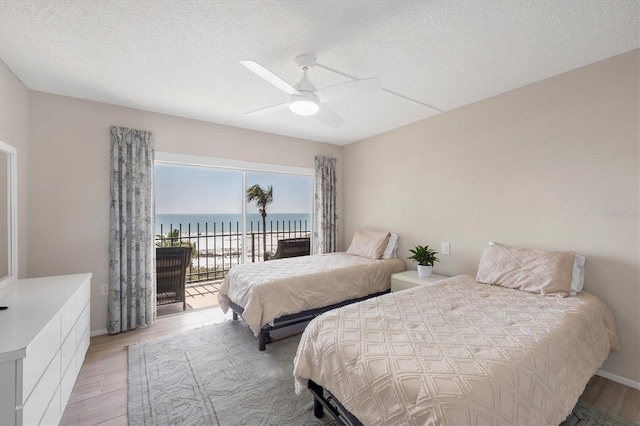 bedroom with a water view, access to exterior, a textured ceiling, light wood-style floors, and ceiling fan