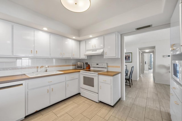 kitchen with white appliances, a sink, white cabinets, under cabinet range hood, and backsplash