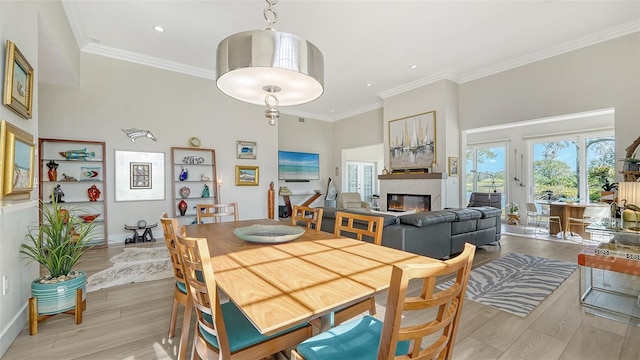 dining room with light wood finished floors, a glass covered fireplace, a towering ceiling, crown molding, and recessed lighting