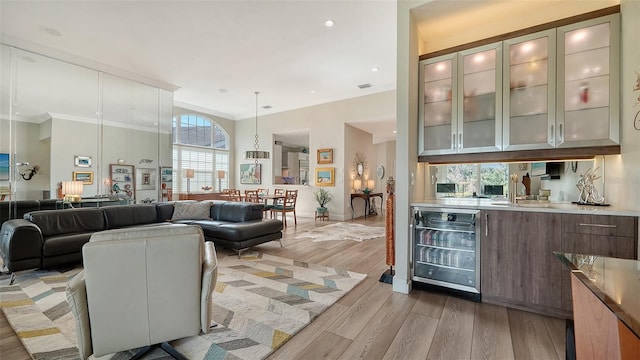 bar featuring beverage cooler, baseboards, light wood-style flooring, ornamental molding, and a sink