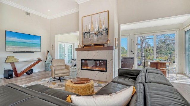 living area featuring crown molding, visible vents, a high ceiling, a high end fireplace, and wood finished floors