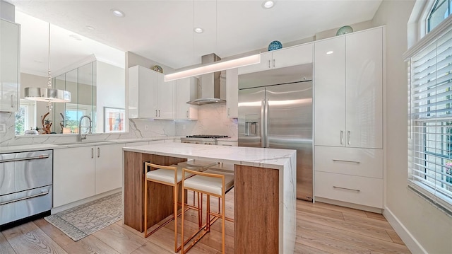 kitchen with appliances with stainless steel finishes, white cabinetry, a sink, and wall chimney range hood