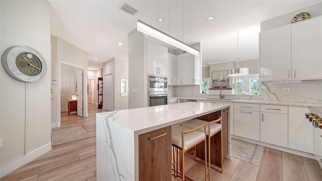 kitchen with stainless steel double oven, light wood-style flooring, a sink, visible vents, and tasteful backsplash