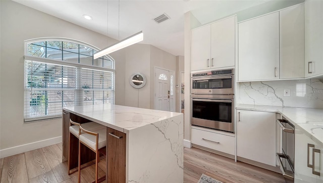 kitchen with a center island, backsplash, appliances with stainless steel finishes, light stone countertops, and light wood-type flooring