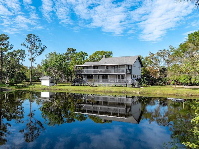 rear view of property featuring a yard, a water view, an outdoor structure, and a storage shed