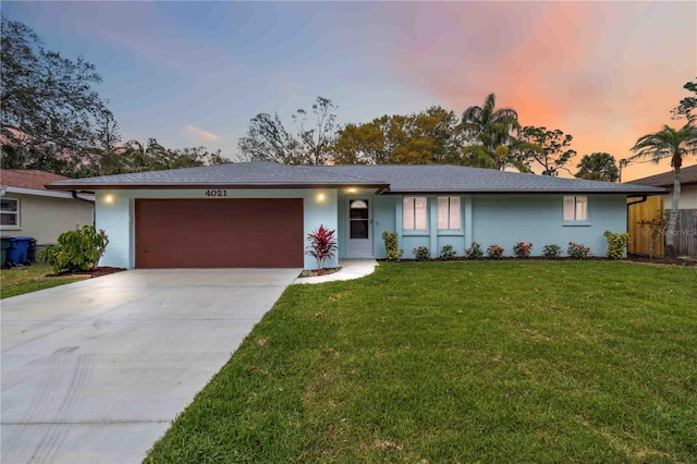 ranch-style house featuring a yard, driveway, an attached garage, and stucco siding