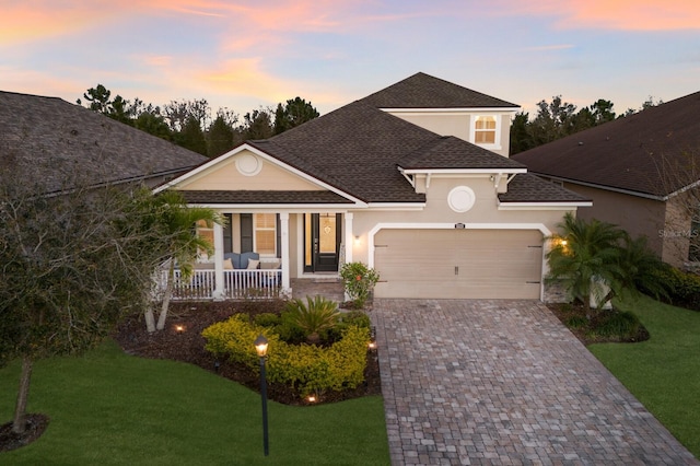 view of front of property with a garage, a shingled roof, a porch, decorative driveway, and a front lawn