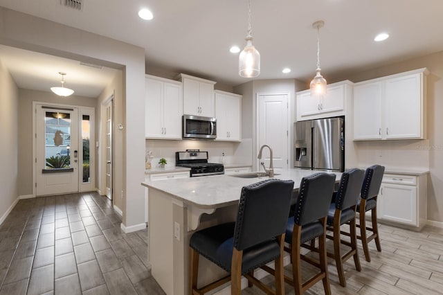 kitchen with stainless steel appliances, white cabinetry, a sink, and a kitchen bar