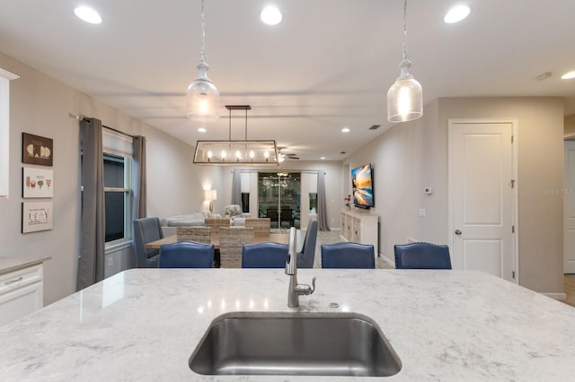 kitchen with recessed lighting, open floor plan, a sink, and light stone countertops