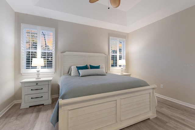 bedroom with a raised ceiling, light wood-style flooring, and baseboards