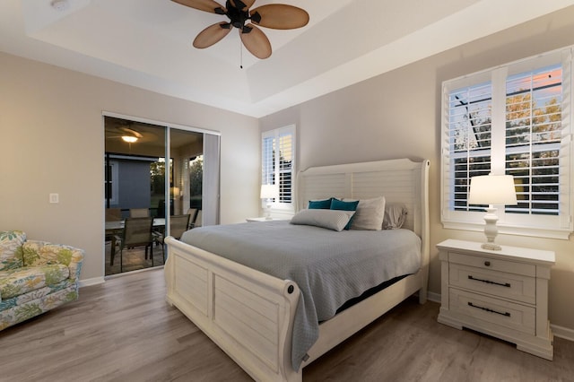 bedroom featuring access to exterior, a raised ceiling, baseboards, and light wood finished floors